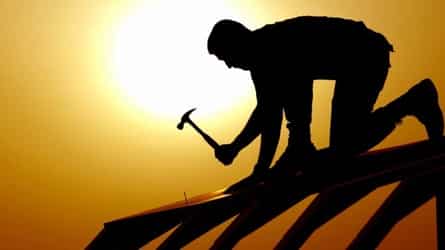 A silhouette of a man with a hammer in his hand, building a house roof