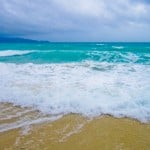 A little wave crashing against the beach, blue and white foamy surf.