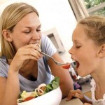a mother feeding her young daughter salad