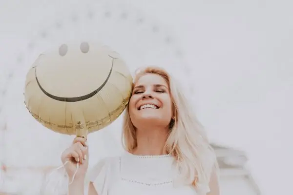 A woman hold a happy face balloon in her hand.